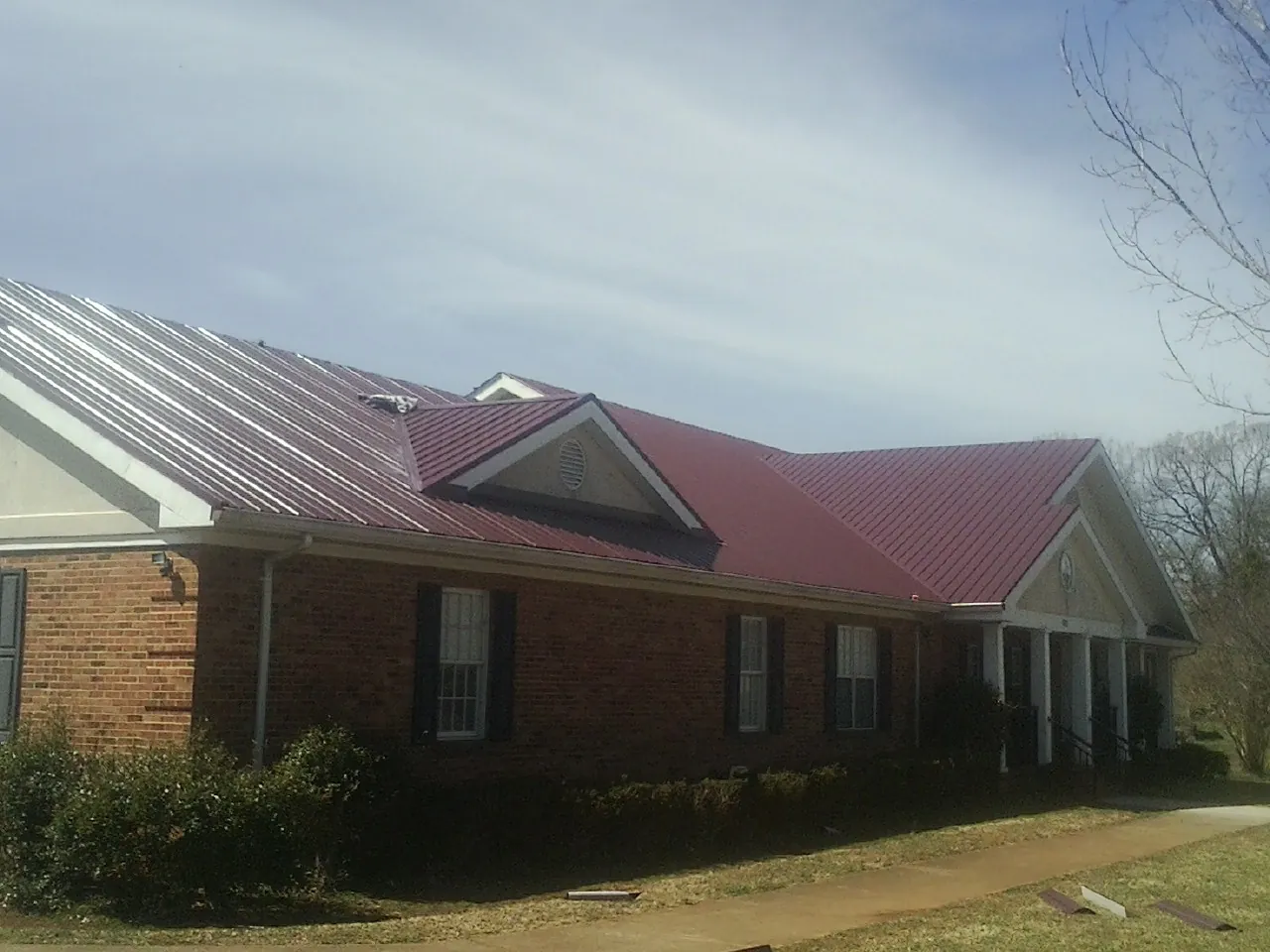 Red metal roof with gabled entries on a long brick building, from a Hail Damage Roof Repair job in Thorntown