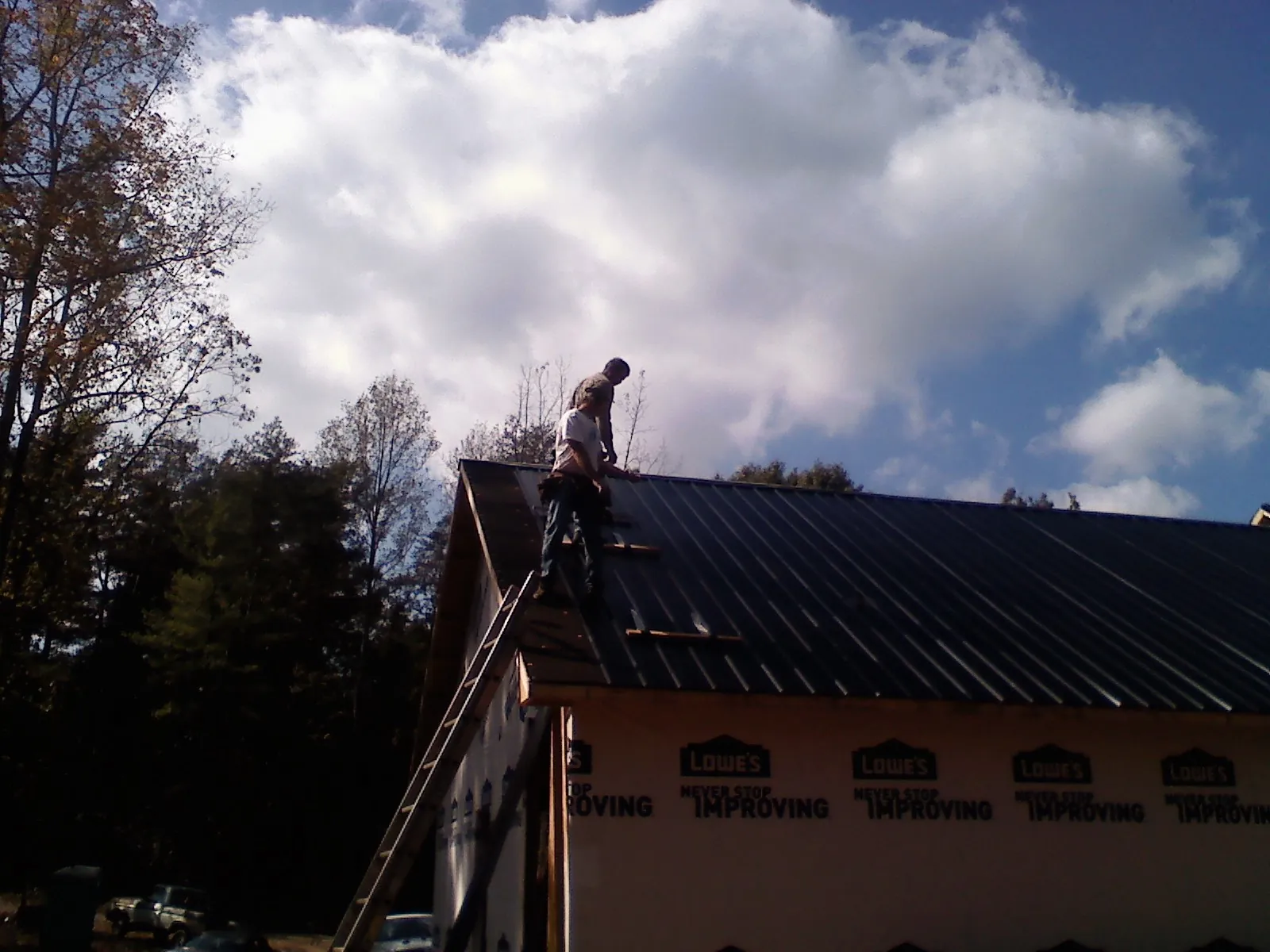 Roofer fastening dark metal panels high against a cloudy sky, from a Roof Inspection job in Thorntown