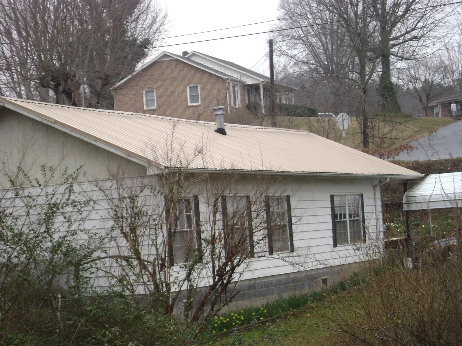 Tan metal roof on a white sided house set into a hillside — Commercial Roofing by Roofing Brothers in Thorntown
