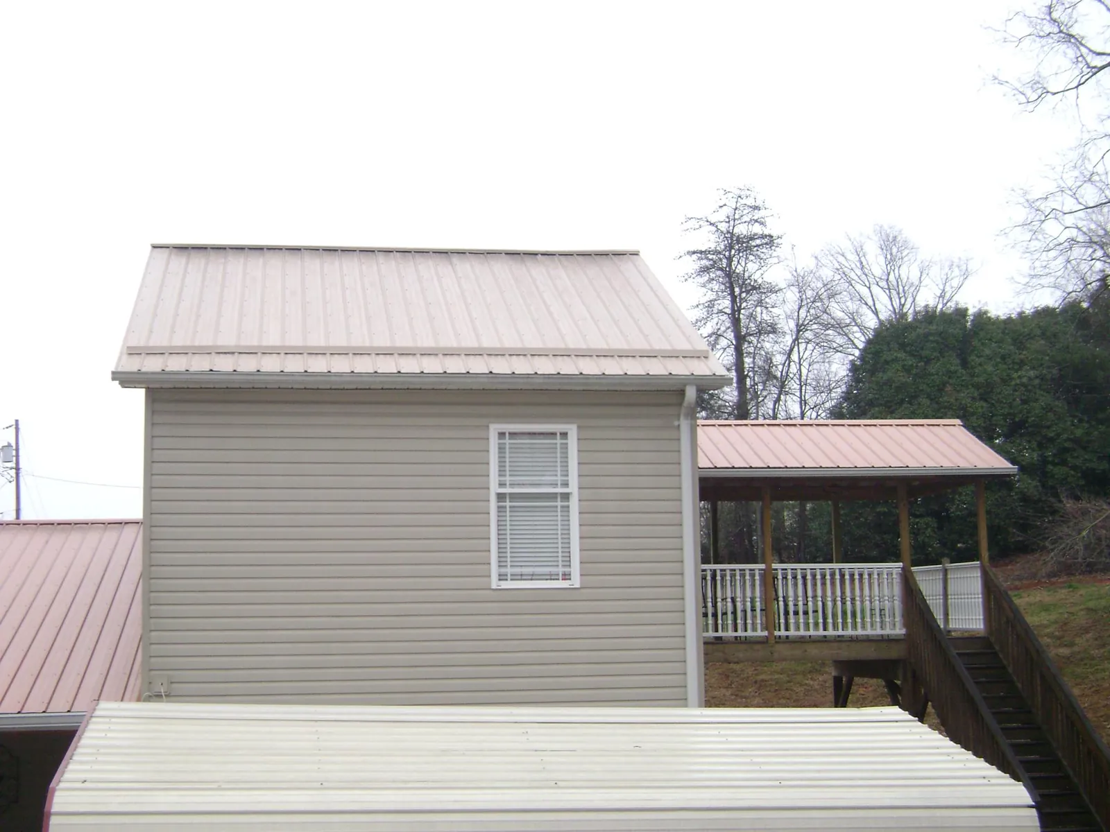 Tan metal roofs on a two story addition and attached porch, from a Roof Replacement job in Thorntown