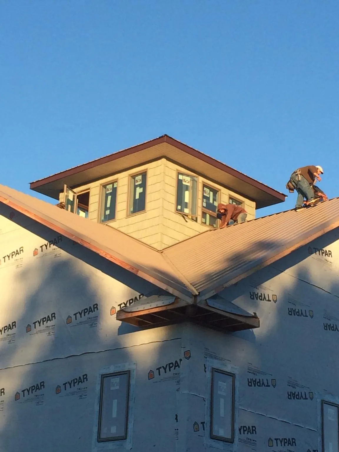 Roofers working around a rooftop cupola on a new metal roof at sunset in Thorntown